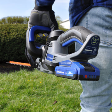 View of hedge trimmer from the back. Focusing on the handle and battery. Hedge and grass in the background