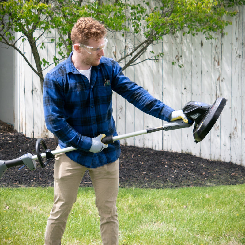 A man holding a string trimmer and edger examines the head of the string trimmer.