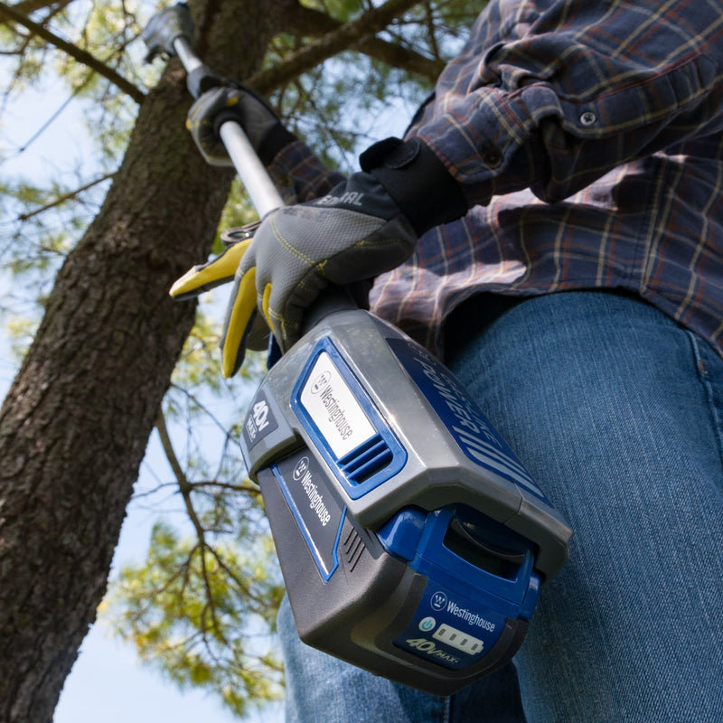 Image from below of someone using the pole saw on a high up tree branch.