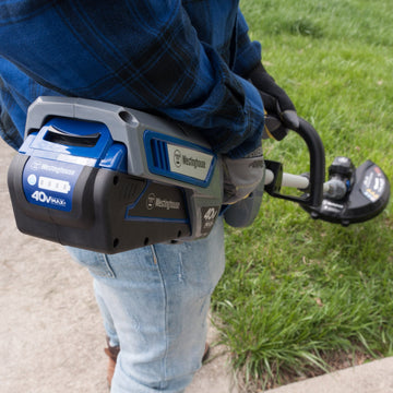 A person uses a 40V string trimmer and edger on the grass. Closeup of the back of the string trimmer showing where the battery plugs in