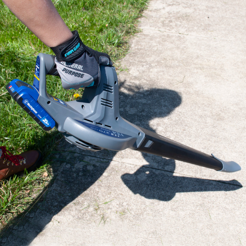 A hand holding a leaf blower on a background of sidewalk and grass