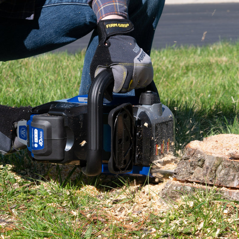 A person cuts away the base of a stump using a chain saw.